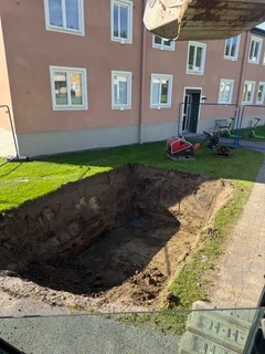 Öppen schaktgrop för underjordsbehållare intill ett flerbostadshus